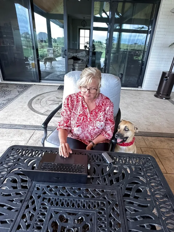 Donnine Souhrada working on her computer on the patio with her dog beside her looking at the screen