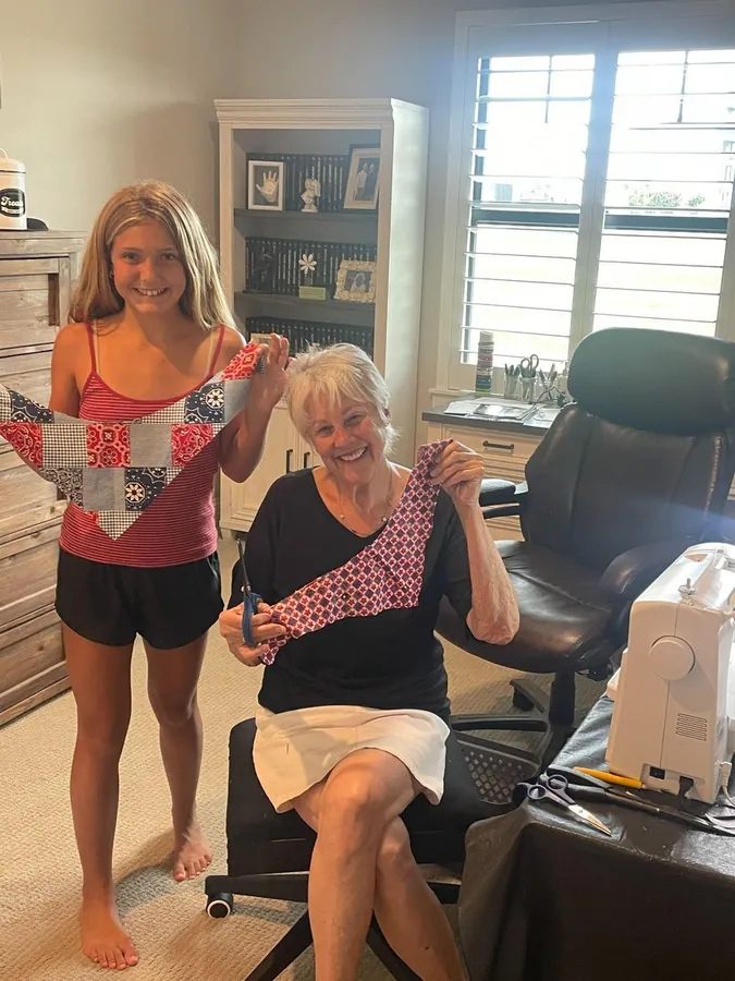 Grandmother and granddaughter holding up finished bandanas in the sewing room, smiling